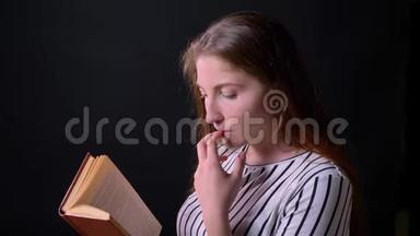 美丽动人的年轻女子阅读书籍和思考，侧写观，在黑色背景上孤立
