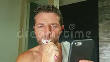 有魅力的网瘾男在家浴室用毛巾擦肩，用牙刷用手机刷牙