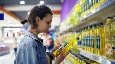 店里的女孩，在一个油瓶上看信息贴纸。 选了一瓶葵花籽油，放在手推车上