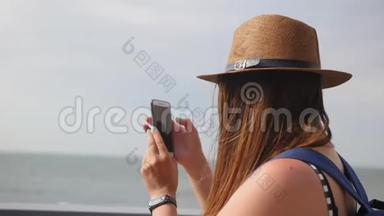 侧景，特写，年轻女孩戴着帽子在夏天的长廊散步，在智能手机上拍照，享受散步