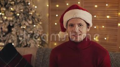 <strong>圣诞老人</strong>戴着<strong>圣诞老人</strong>的<strong>帽子</strong>看着圣诞树背景上的摄像机的微笑迷人男人的肖像。 慢动作