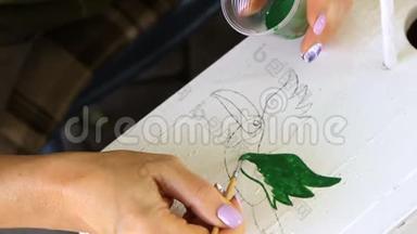 女人在一个木制的<strong>筑巢</strong>箱上画着一只绿鸟的轮廓，它与葡萄的绿叶交织在一起
