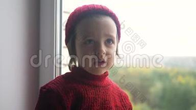 穿着红色毛衣和针织帽子的男孩坐在白色的大窗户上