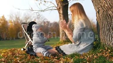 年轻的妈妈坐在草地上和她的小宝宝玩.. <strong>拍手</strong>。 阳光。