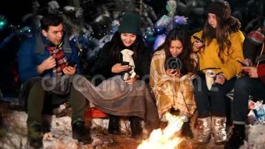 冬天森林里的年轻人坐在火边。 人们坐在手机里微笑。 <strong>社会问题</strong>