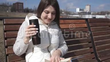 公园里一个穿着运动服的漂亮女孩坐在长凳上看书，喝着热杯子里的咖啡。<strong>大笑</strong>