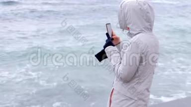 穿白色夹克的女人拿着手机<strong>大风</strong>浪。 后景。