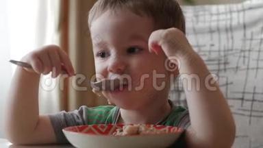 可爱的小宝宝一个人用勺子从盘子里吃粥，健康饮食的概念。