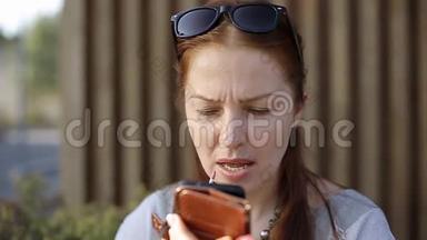 一位中年妇女坐在街头咖啡馆的餐桌旁，用智能手机<strong>而不是</strong>智能手机涂口红