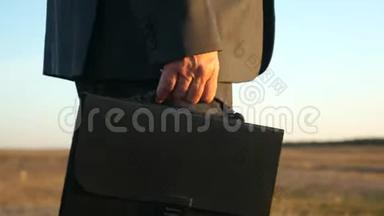 一个身穿商务服，手里拿着黑色公文包的人正在公园里散步。 特写