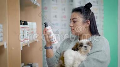 一位年轻的女宠物主人正在一家商店里为她的狗挑选洗发水，手里拿着可爱的狮子狗