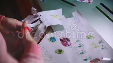 一个可爱的小女孩的特写镜头`她用剪刀在桌子上从一张纸上剪出手绘图片。