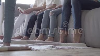 妈妈和她儿子的腿。 女人和三个穿牛仔裤的男孩坐在靠近对方的沙发上。 第四次
