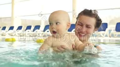 可爱的婴儿抱着妈妈正在<strong>游泳</strong>池里<strong>学习游泳</strong>。 这孩子把手溅在水上
