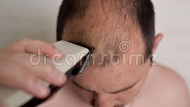 光头男在浴室里用电动剃须刀刮头发。 美容护理，美容