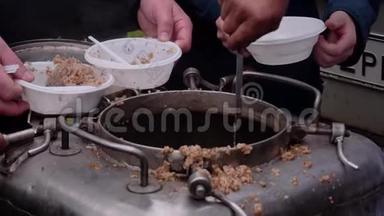 厨师把一个大锅炉里的粥放在人们手中的塑料盘子里。 现场厨房的特写..