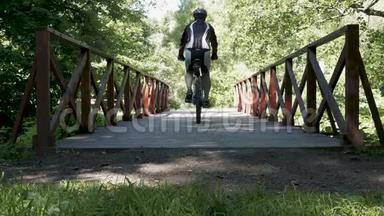 一个人骑着自行车沿着公园里的一座桥行驶。 在夏天。