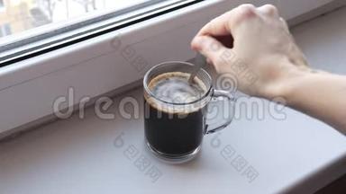 女人早上在窗台上的透明玻璃杯里煮速溶咖啡，<strong>用勺子</strong>搅拌