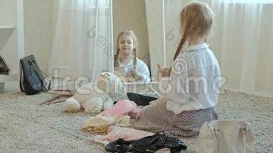 穿着粉红色裙子扎着辫子的开朗女孩试着穿着成年妈妈`衣服、连衣裙、高跟鞋和在前面跳舞