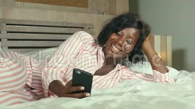 美丽的美国黑人女士，穿着睡衣，躺着，轻松的微笑，愉快的，新鲜的使用互联网手机网络