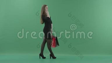 美丽快乐的女人穿着黑色的小裙子，摆着购物袋，笑着。 她站在工作室里