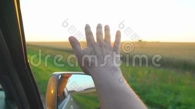 日落时分的人手。 一个人在阳光下从车窗`手，在大自然的背景景观上看到阳光。 荣耀