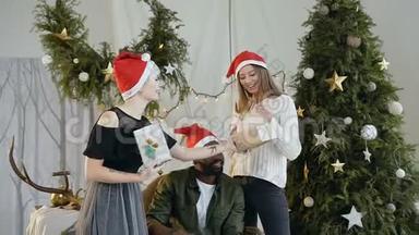 戴着圣诞老人帽子的年轻一对快乐的人在圣诞老人的背景下愉快地向他们的朋友赠送礼物