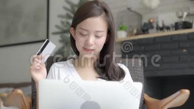 美丽的肖像年轻的亚洲妇女在网上购物，用笔记本电脑上网，坐在家里的客厅里