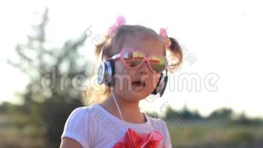 戴耳机的搞笑孩子听音乐，唱歌，跳舞.. 夏天日落时戴太阳镜的可爱女孩。