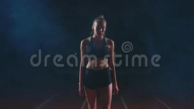一位身材苗条的女运动员穿过烟雾，看着摄像机，走近比赛的起跑线