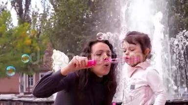 妈妈和女儿在玩肥皂泡。 妈妈带着一个小孩在喷泉里充气肥皂泡。