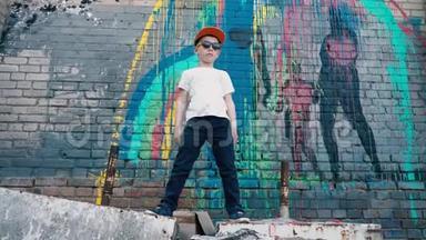 一个很酷的5岁孩子戴着墨镜在砖墙边跳着涂鸦，一个年轻的街头舞者，