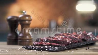 切片烤肉放在黑摊上.. 厨师用手撒胡椒和盐。 特写，慢动作..