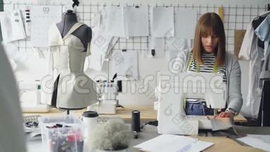 自谋职业的服装设计师正在使用缝纫机，缝制纺织品，并查看躺在上面的草图
