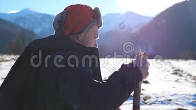 山背景下，年轻的徒步旅行者在雪地小径上用棍棒行走，在野外的侧面观看。 运动男