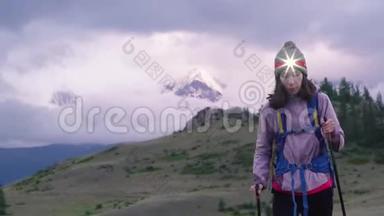 晚上，一个带着背包、前照灯和徒步旅行棒的女孩在<strong>山里</strong>旅行。 山谷，低矮
