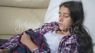 一个十几岁的<strong>女孩</strong>在家里的沙发上<strong>感冒</strong>了，她用毯子盖住自己，测量温度。