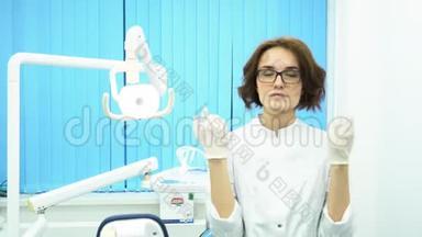 年轻的女医生戴着眼镜和一件白色的外套，在牙科诊所的戴上白色的医疗手套。 严格的