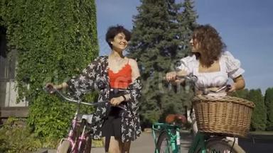 两个穿着鲜艳衣服的积极的女人在街上狭窄的路上牵着自行车说话。 农村生活