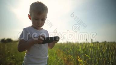 小男孩站在田野的中央，使用智能手机，玩游戏，发布照片。 有趣，现代的孩子