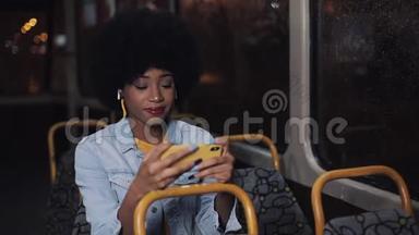 年轻的非洲裔美国妇女在<strong>公共交通工具</strong>上看智能手机视频。 晚上。 特写镜头。 城市