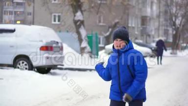 穿蓝色羽绒服的少年扔雪球。 冬天，下雪了