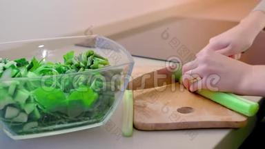 特写镜头，动作缓慢，无法辨认的女人把芹菜片放在木板上，放入一个大厨房的玻璃沙拉碗里