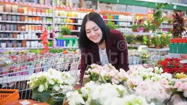 <strong>美丽</strong>的<strong>深色</strong>头发的年轻女子在花园商店超市里闻着鲜花，女园丁手轻轻地抚摸着