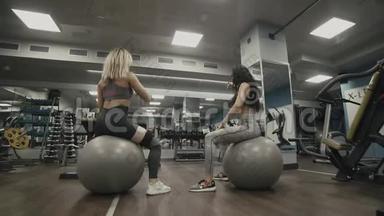 两名年轻运动员坐在健身房的训练球上。 穿运动服装的女人
