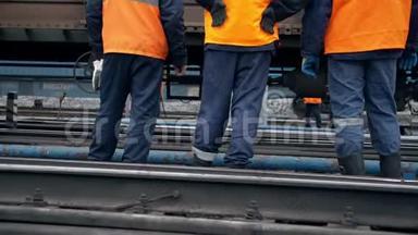 铁路工人正站着看着一列经过的火车。腿部特写。穿着橙色工作服的工人