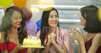 年轻女子的生日女孩正在许愿，在蛋糕上吹蜡烛，在朋友祝贺时拍手