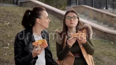 两个女孩坐在公园里吃披萨和鸡肉聊天