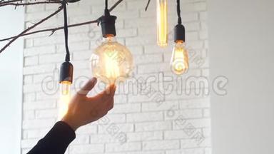 人的手掌`白色砖墙在灯光室里触摸大灯泡。 媒体。 电力