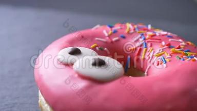 特写上景的美味的粉红色甜甜圈与五颜六色的薯片和眼睛慢慢旋转在灰色的桌子背景。